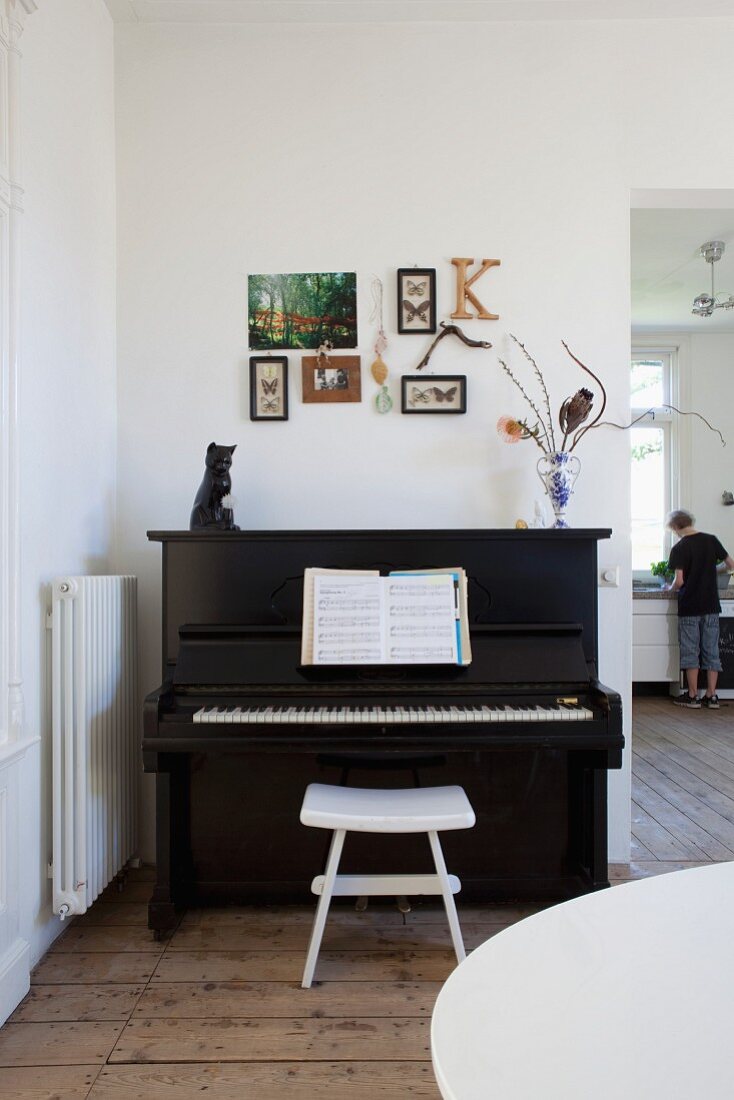 Pictures, letter K and framed butterflies on wall above piano with cat ornament and flowers on top