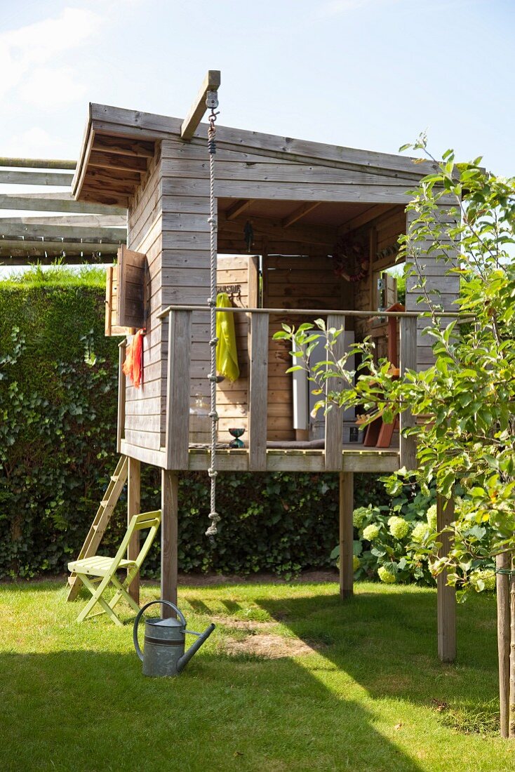 Wooden playhouse on stilts with climbing rope in garden of holiday home