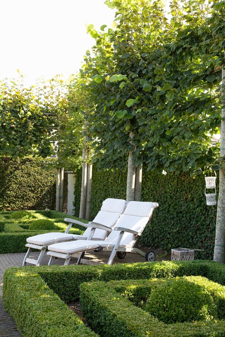 Two deckchairs amongst topiary box hedges in garden surrounded by espalier trees and tall hedges