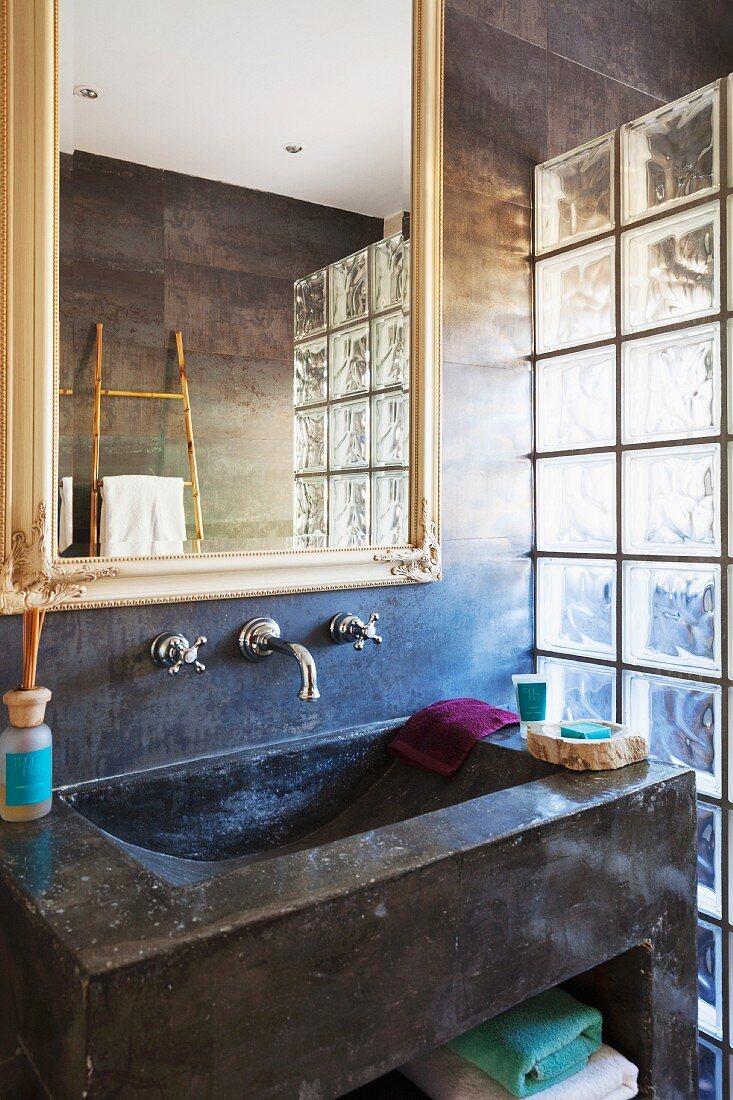 Betonwaschbecken und Spiegel an dunkel marmorierter Wand; seitlich Abtrennung aus Glasbausteinen