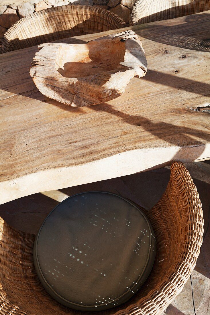 Naturbelassene Holzschale auf rustikalem Tisch und Rattansessel im Sonnenlicht