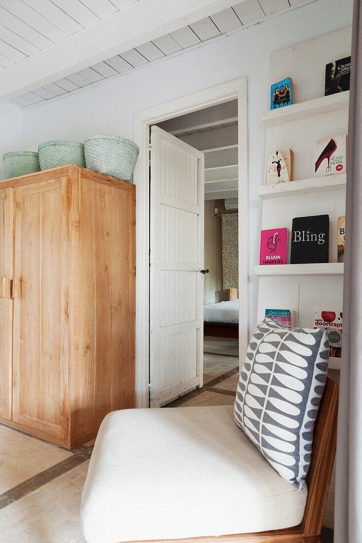 Chair with patterned scatter cushion in front of bookcase and simple wooden cupboard in Mediterranean bedroom