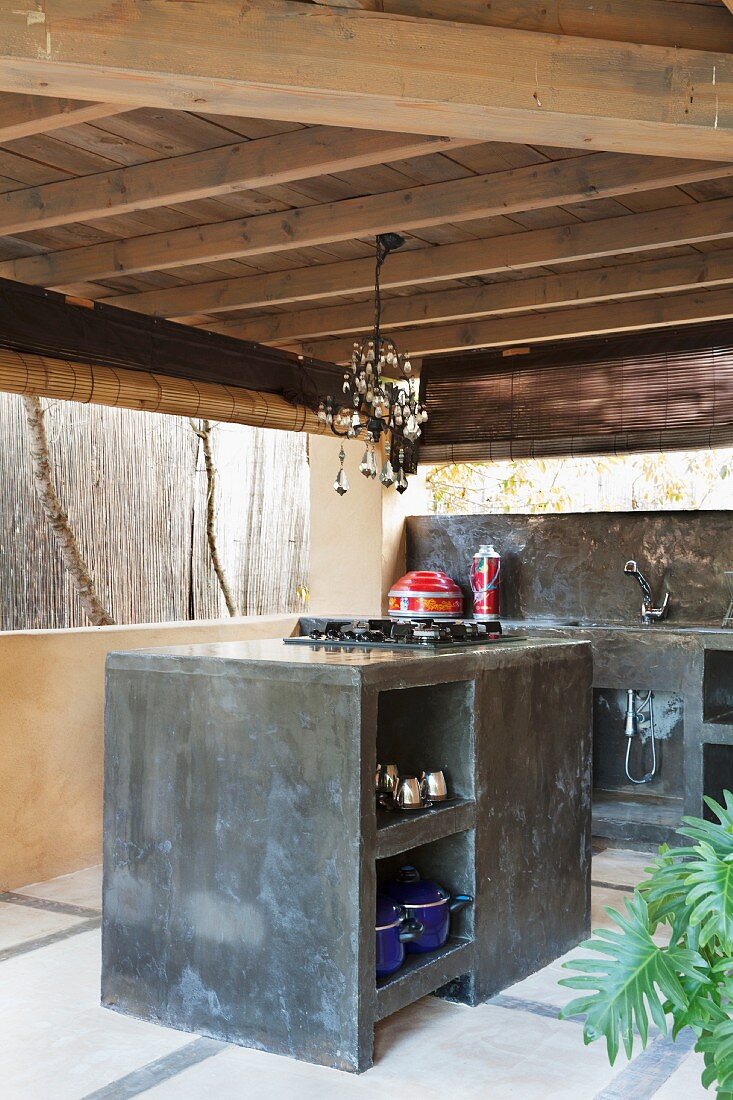 Holzüberdachte Aussenküche aus dunkel marmoriertem Beton mit Glasleuchter über dem Herdblock