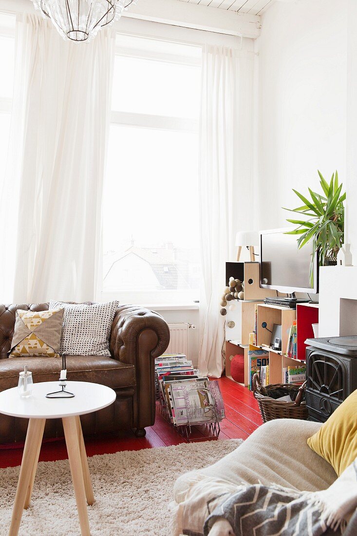 Side table on flokati rug in front of leather couch, airy curtains on windows in comfortable living room