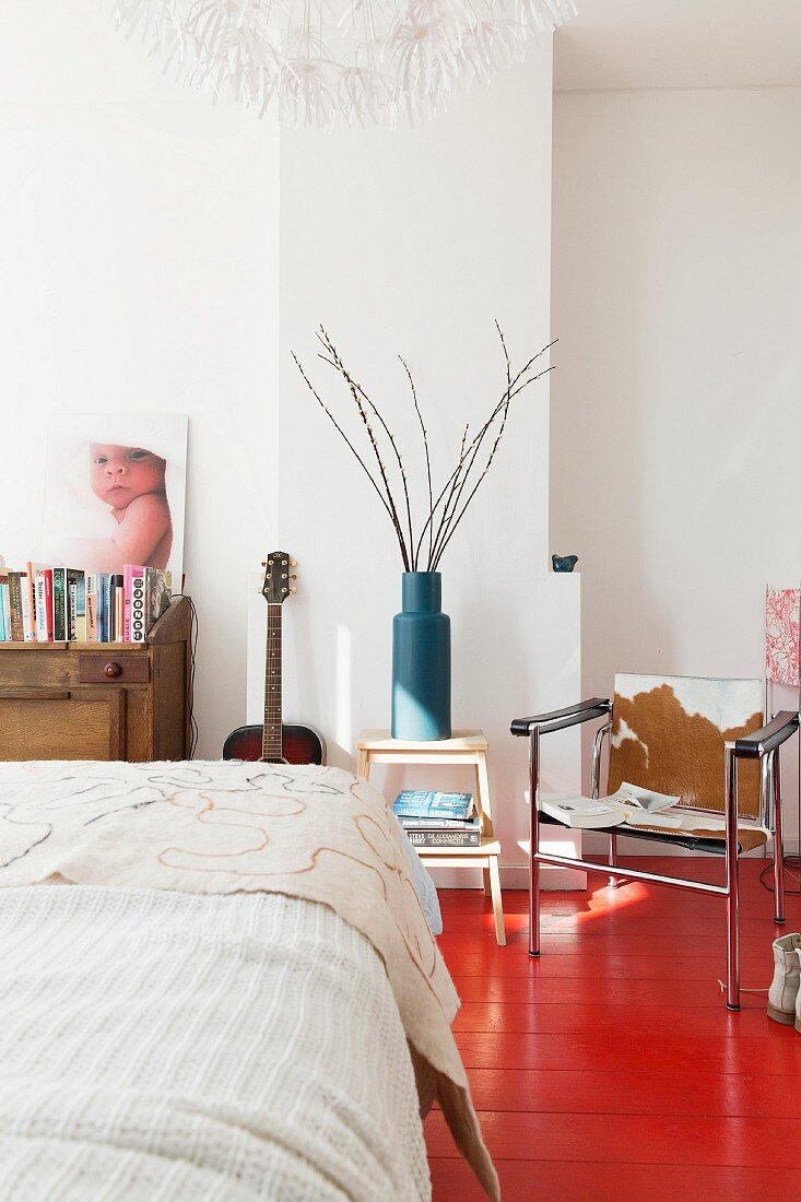 Bett mit weisser Tagesdecke vor Stuhl mit Fellbezug auf rot lackiertem Dielenboden