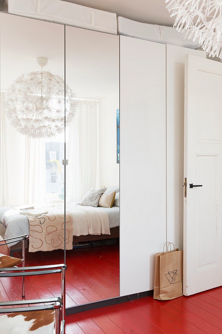 Wardrobe with mirrored doors in bedroom with red-painted wooden floor