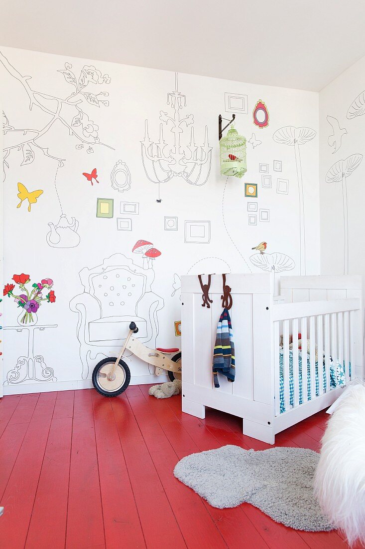 Weisses Kinderbett auf rot lackiertem Dielenboden, an Wand Tapete mit Zeichnungen