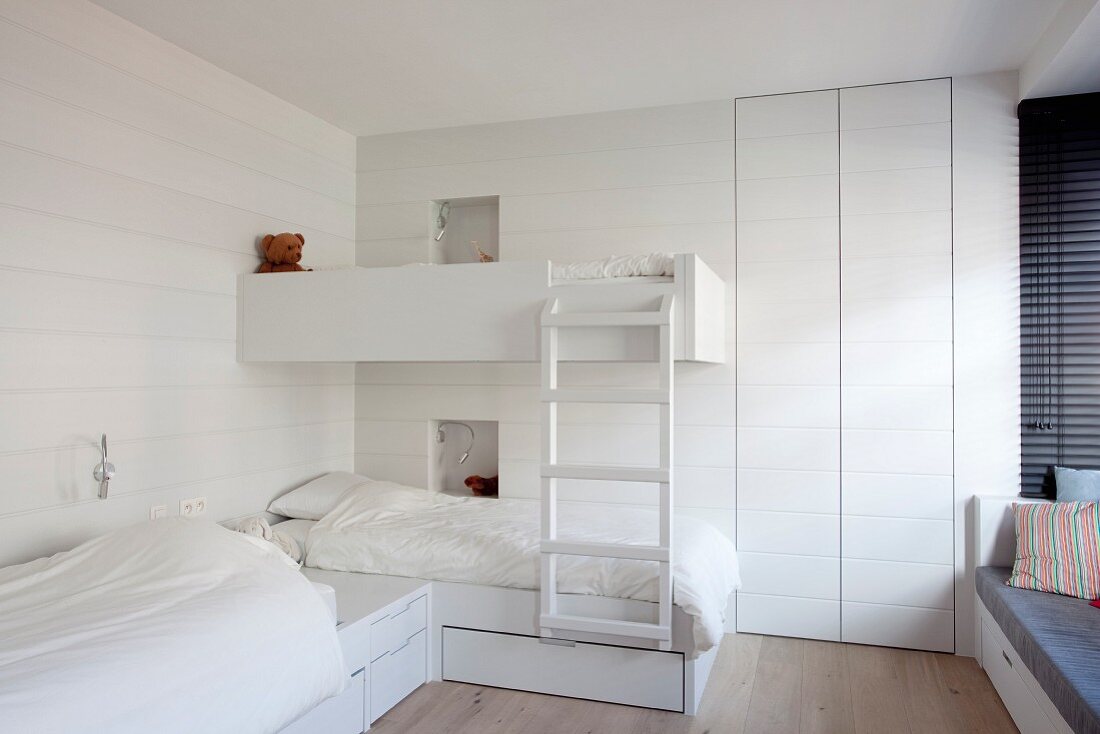 Two beds arranged in an L and one loft bed in children's bedroom painted white