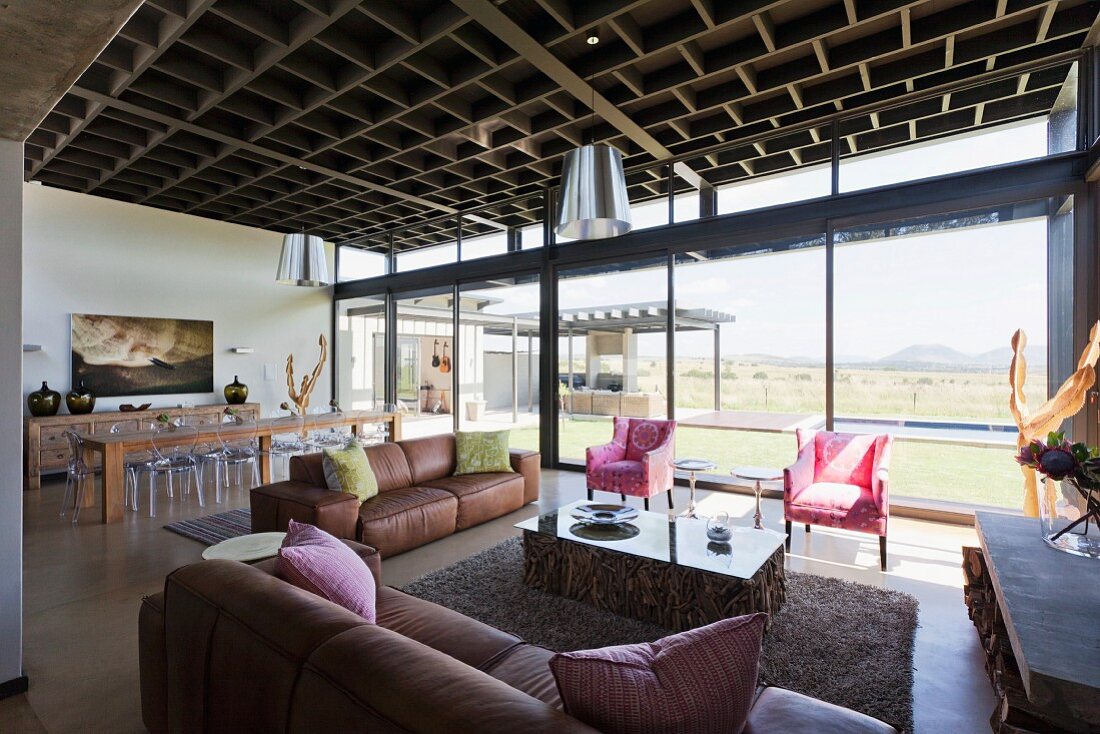 Offener Wohnraum mit Loungebereich vor verglaster Fassade mit Landschaftsblick, kassettenartige Decke in zeitgenössischem Wohnhaus