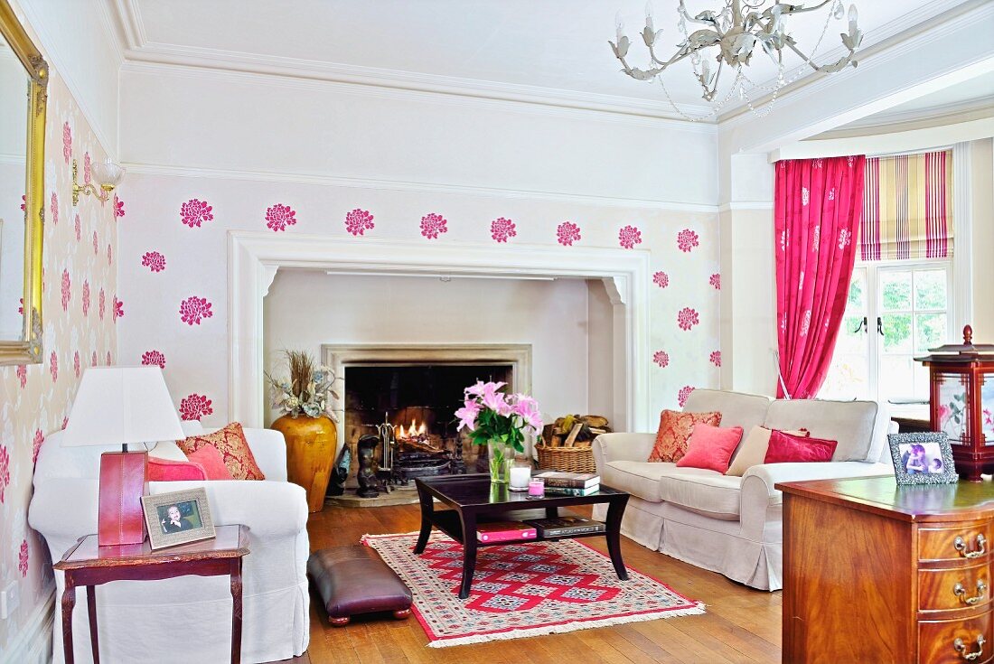 Wohnzimmer mit Pink Akzenten, weiße Sofagarnitur und schwarzer Couchtisch vor offenem Kamin
