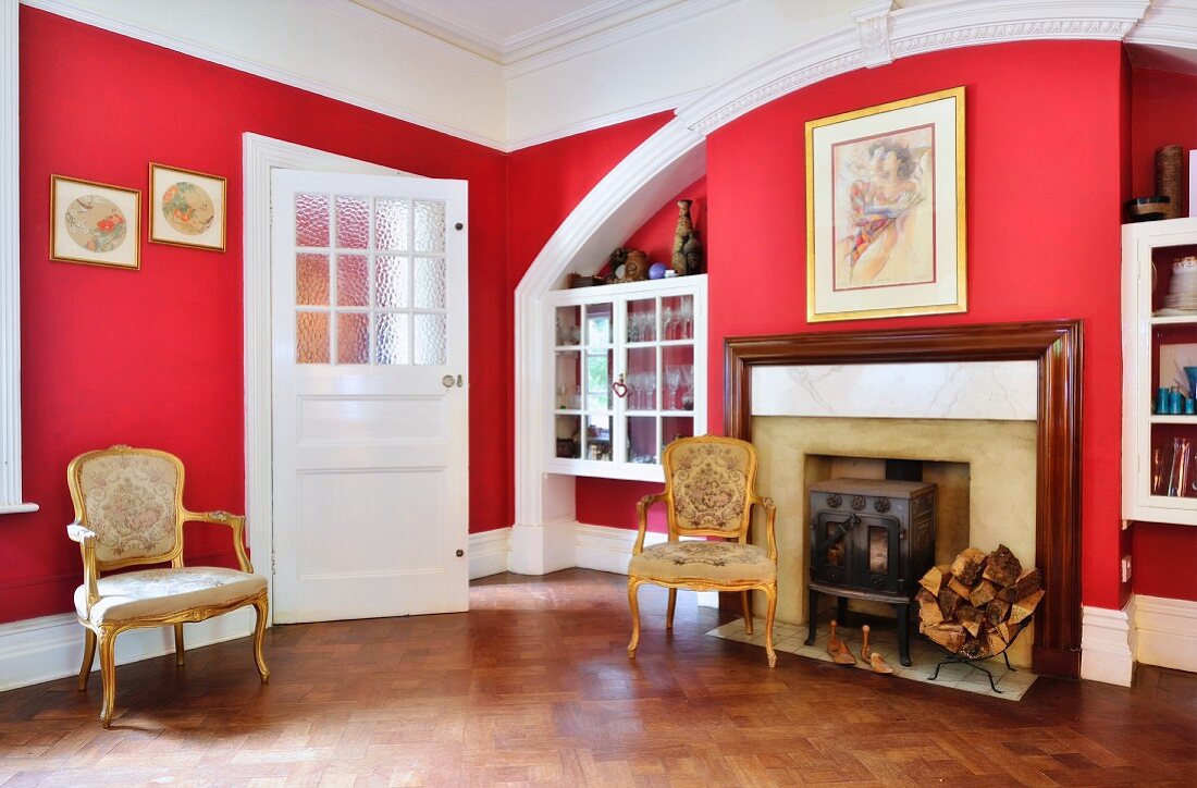 Gemauerter Rundbogen mit integriertem Kamin, eingebaute Vitrinenschränke, davor vergoldete Rokoko Stühle im Zimmer mit roten Wänden