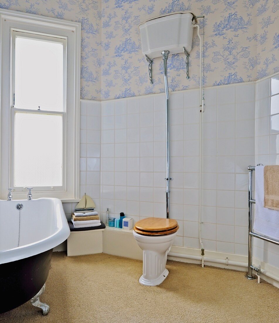 Toilette mit Vintage Spülkasten und freistehende Badewanne im Badezimmer mit Toile-de-jouy Tapete und weissen Wandfliesen