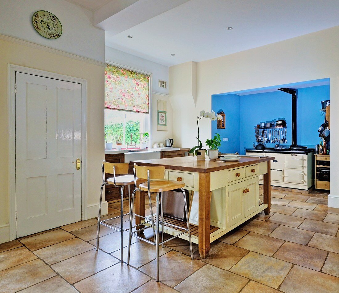 Freistehender Küchenblock mit modernen Barhockern, im Hintergrund Küchenherd in blau getönter Nische, in offener Küche