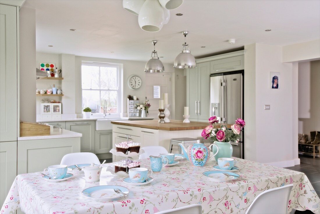 Gedeckter Frühstückstisch mit hellblauem Geschirr, im Hintergrund offene Küche im Landhausstil