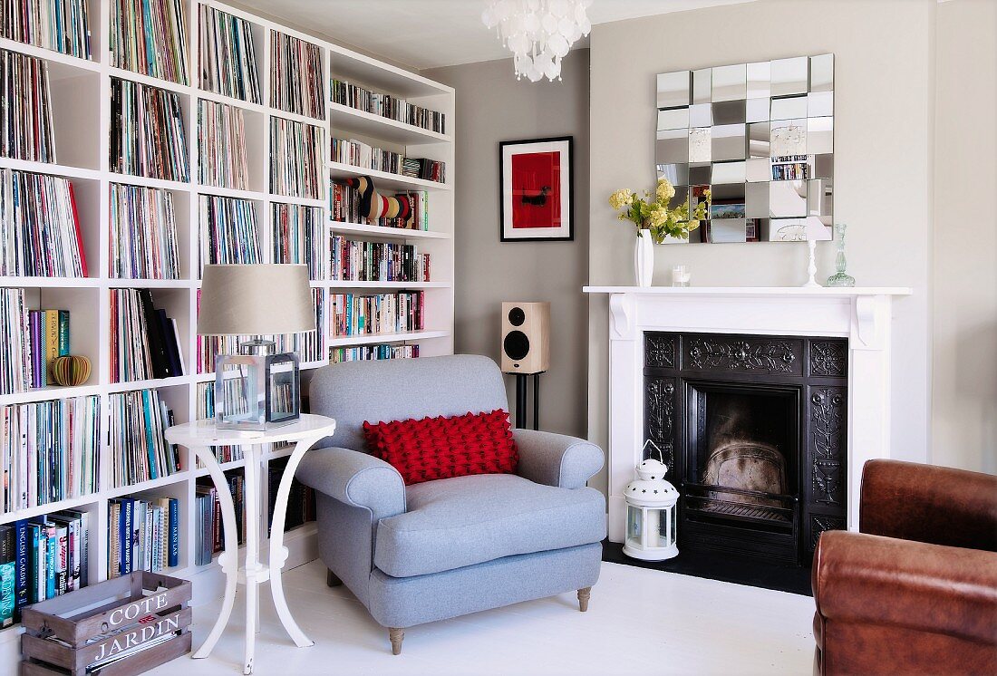 Pale blue armchair and round side table next to open fireplace and white bookcase against wall
