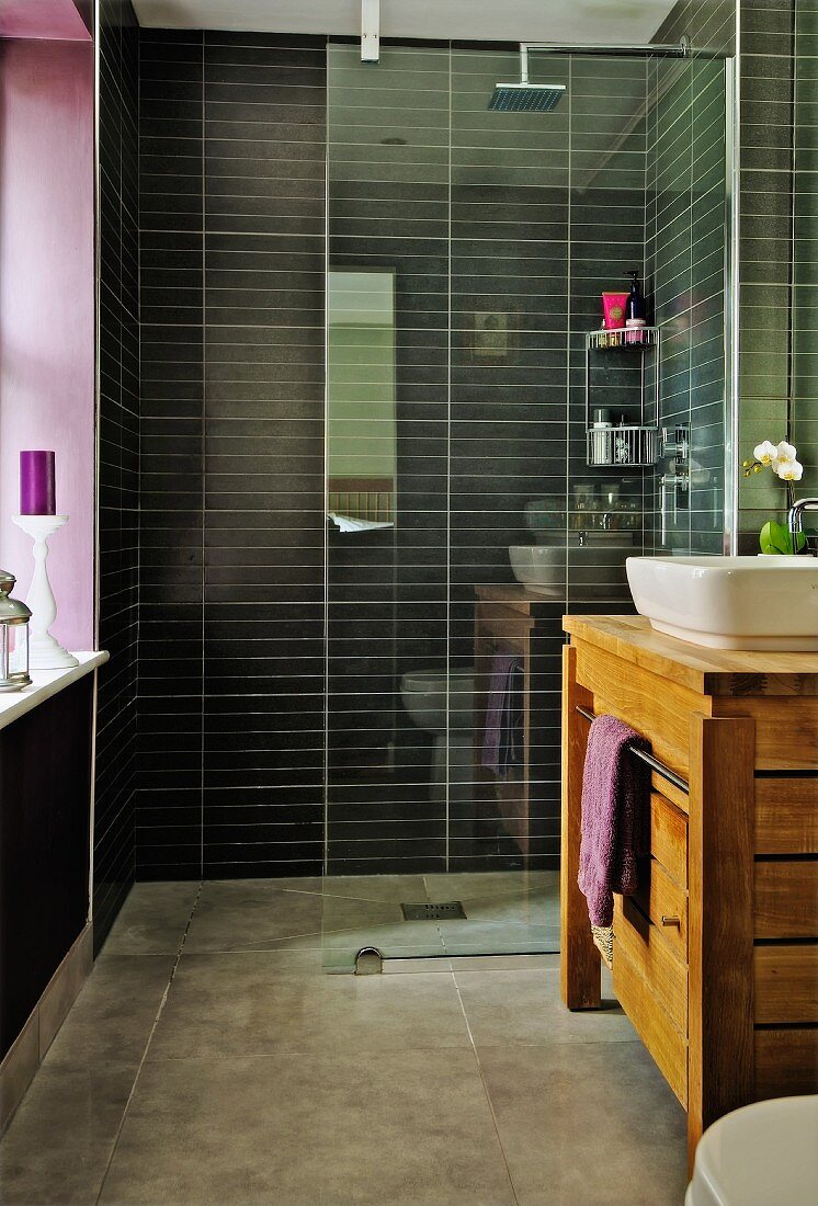 Modern bathroom, glass partition screening shower area with black wall tiles and solid-wood washstand