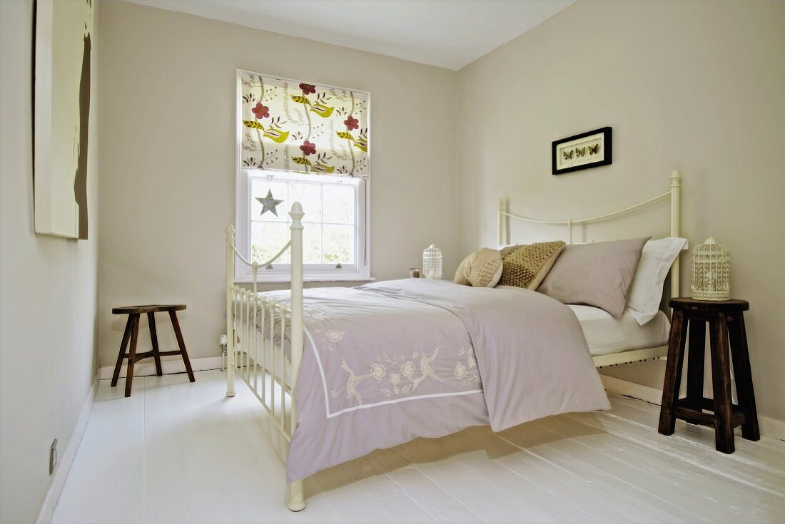 Doppelbett mit weißem, antikem Metallgestell in hellgrau getöntem Schlafzimmer, im Hintergrund Sprossenfenster mit gemustertem Rollo