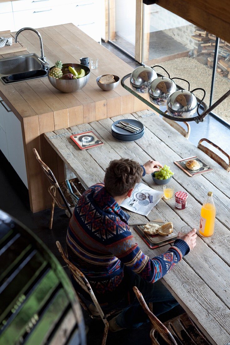 Blick auf Mann an rustikalem Holztisch mit Frühstück in renoviertem Landhaus