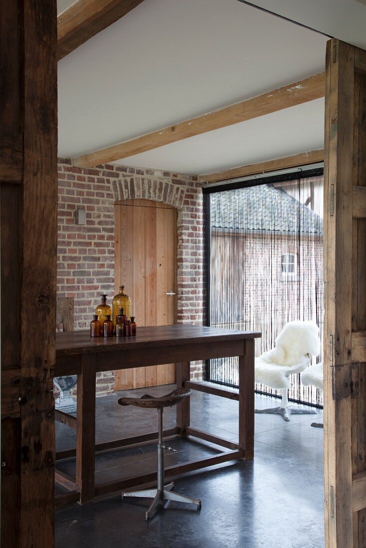 Vintage Barhocker vor schlichter Holztheke in renoviertem Landhaus mit sichtbarer Ziegelwand