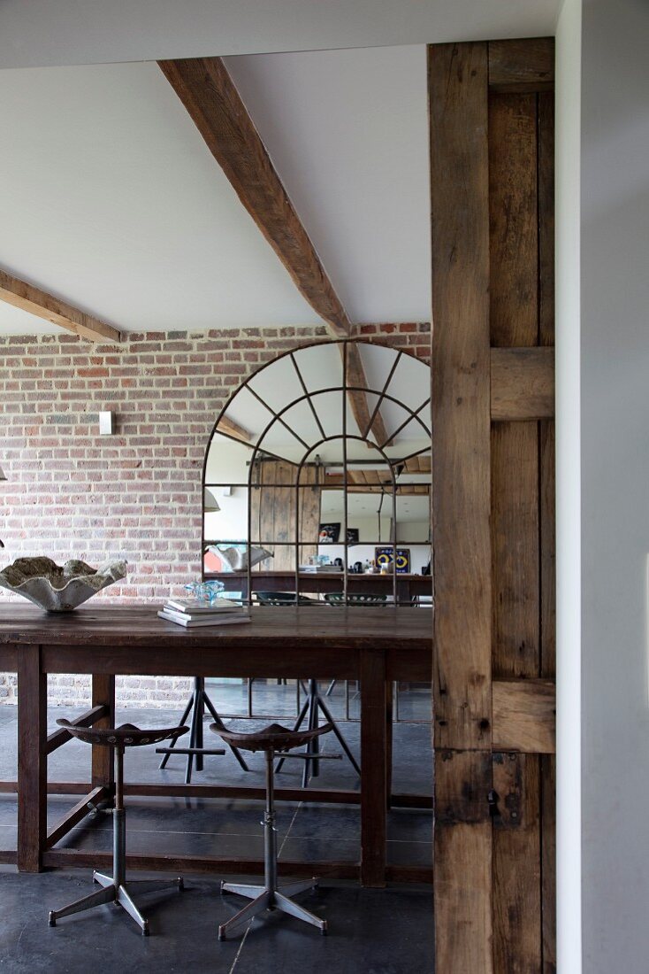 Vintage bar stools at wooden counter in front of arched mirror on brick wall