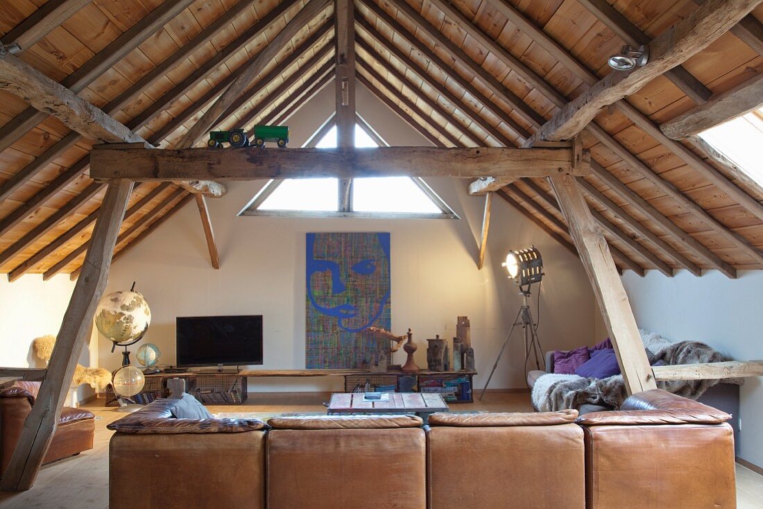 Braune Ledercouch in Loungebereich mit sichtbarer Holzdecke und künstlerischem Flair