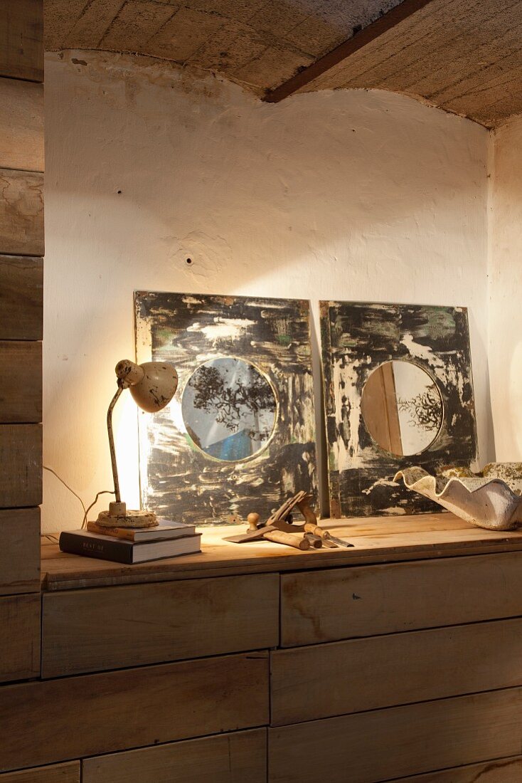 Artistic mirrors on sideboard lit by retro table lamp