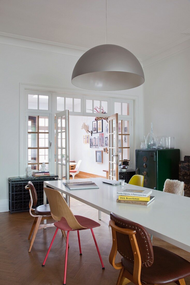 Stühle in Stilmix um weissen Esstisch und Designerleuchte im Esszimmer mit Sprossentür