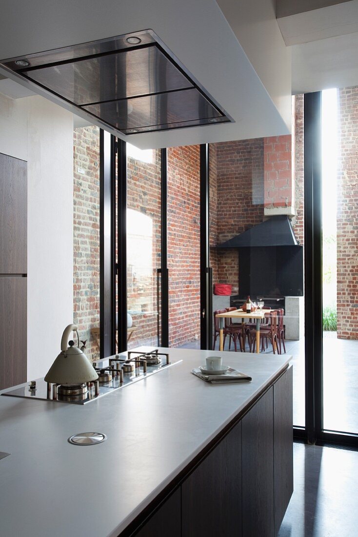 Kitchen counter below extractor hood; glass wall with view into dining area with brick wall in background
