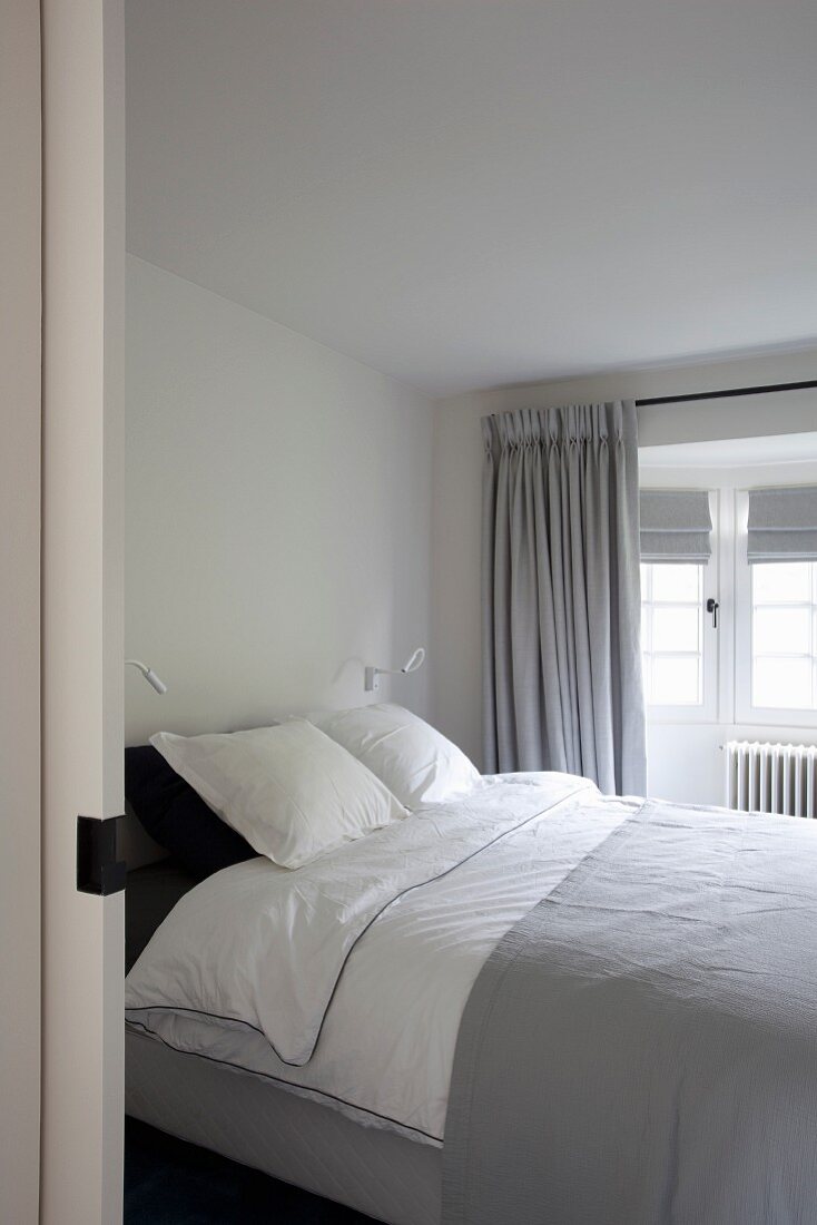 Blick durch offene Schiebetür auf Doppelbett in grau-weisses Schlafzimmer