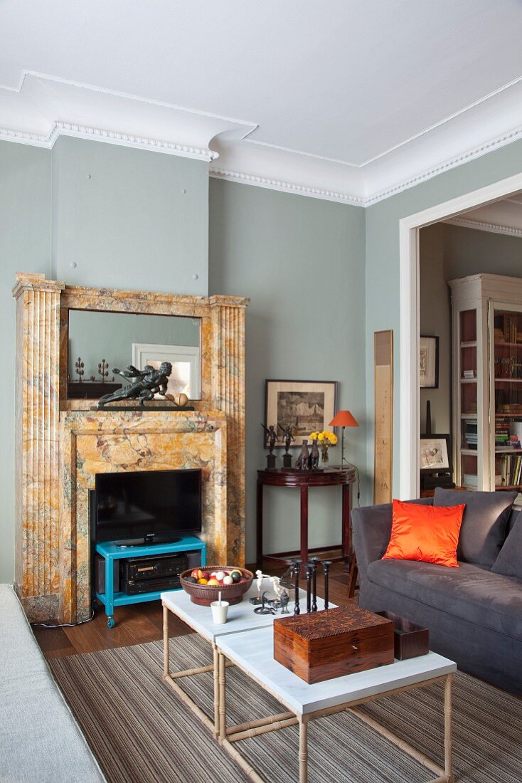 Filigrane Couchtische gegenüber offenem Kamin, in elegantem, grau getöntem Wohnzimmer, mit umlaufendem Stuckfries an Decke