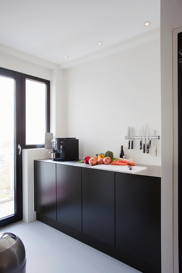 Minimalist kitchen counter with black doors and knives on magnetic bar on wall