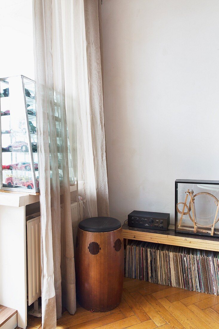 Vintage Lautsprecher aus Holz vor Schallplattensammlung unter Ablage in Zimmerecke, seitlich Glaskasten mit Modellautos hinter Vorhang auf Fensterbank