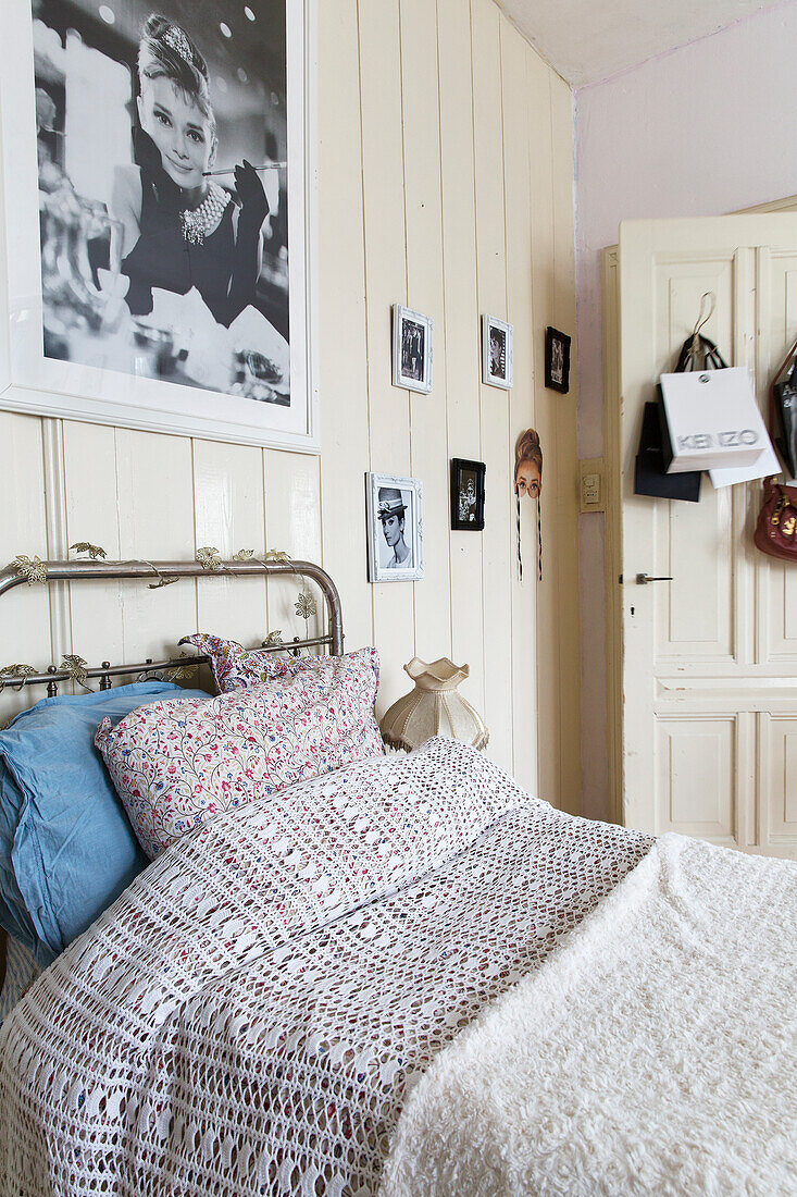 Vintage bed with metal frame below black and white photos on white wooden wall