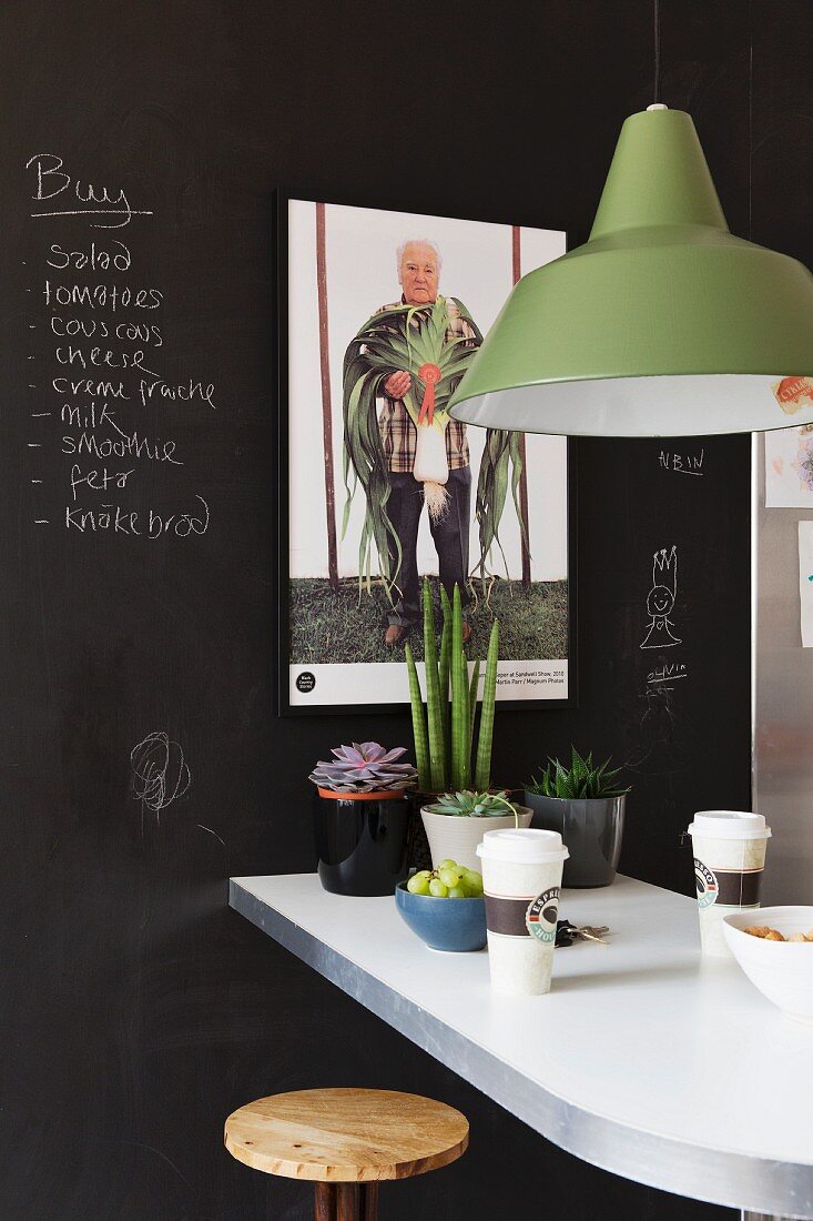 Pendelleuchte mit grünem Metallschirm über Frühstückstheke, vor schwarzer Wand mit Tafellack