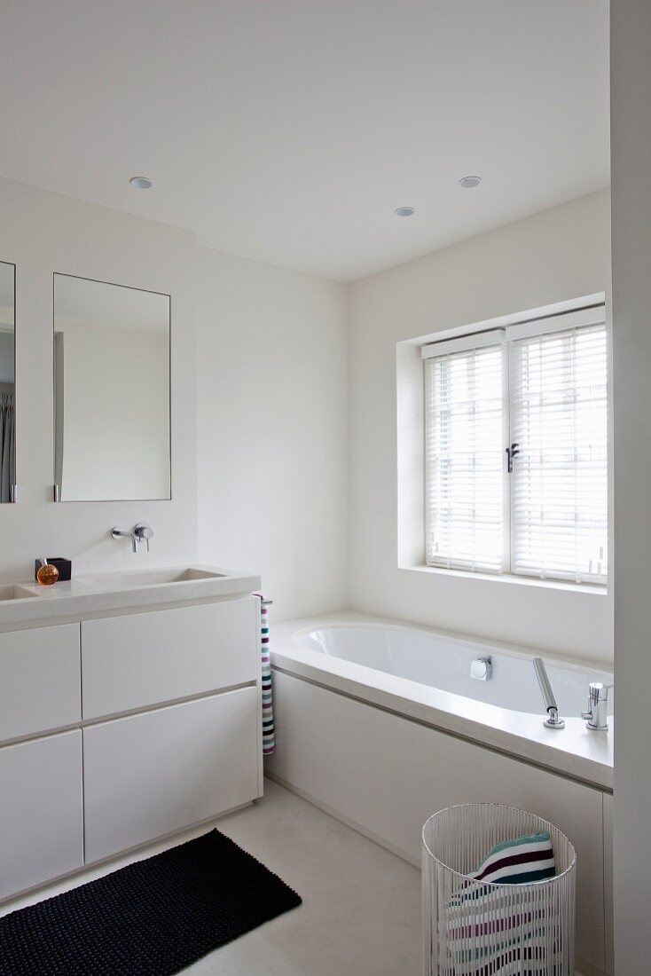 Washstand with white base unit next to bathtub below window in contemporary bathroom