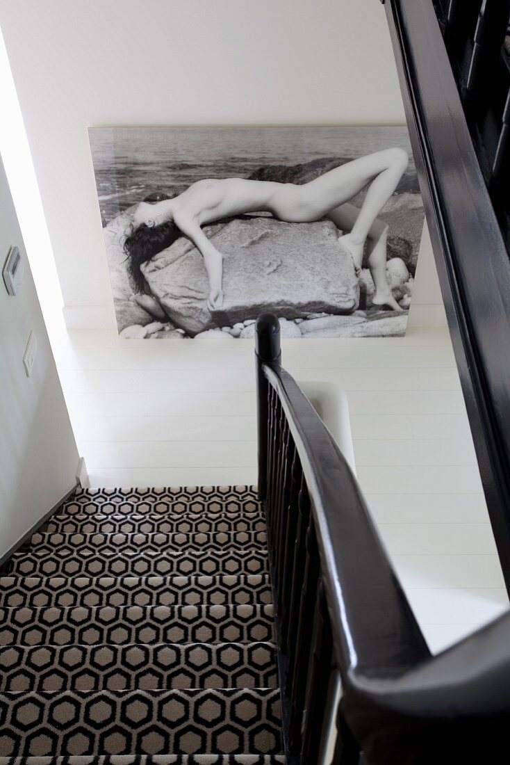 View down staircase with lack and white, geometric carpet and large picture on wall