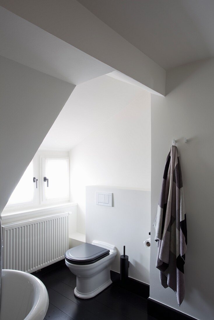 Toilette in weißem Badezimmer mit schwarzen Dielenboden unter dem Dach