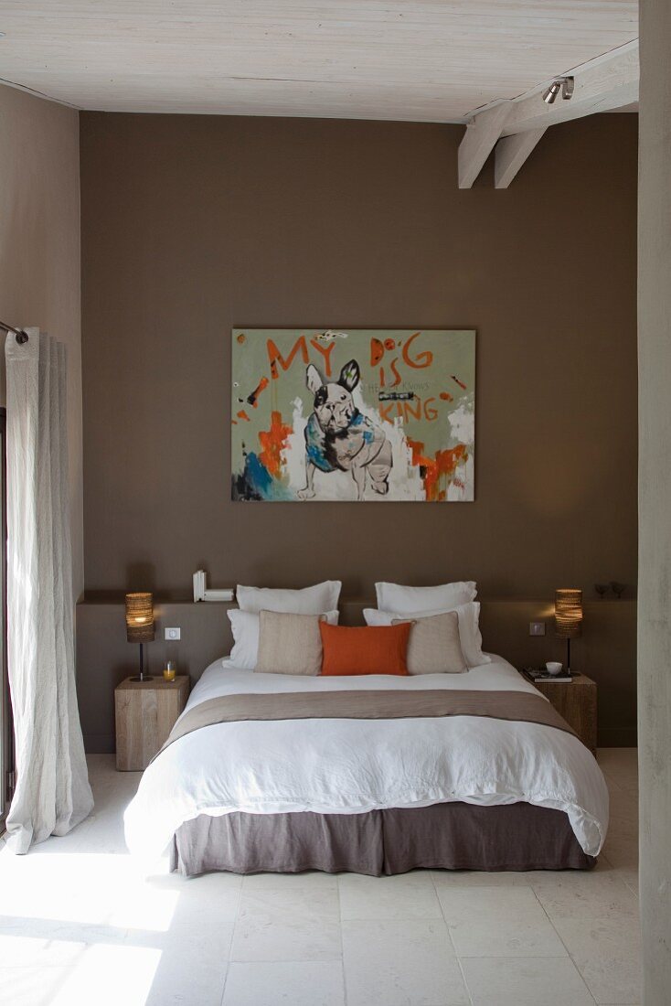 Scatter cushions on double bed below modern artwork and masonry shelf on brown back wall