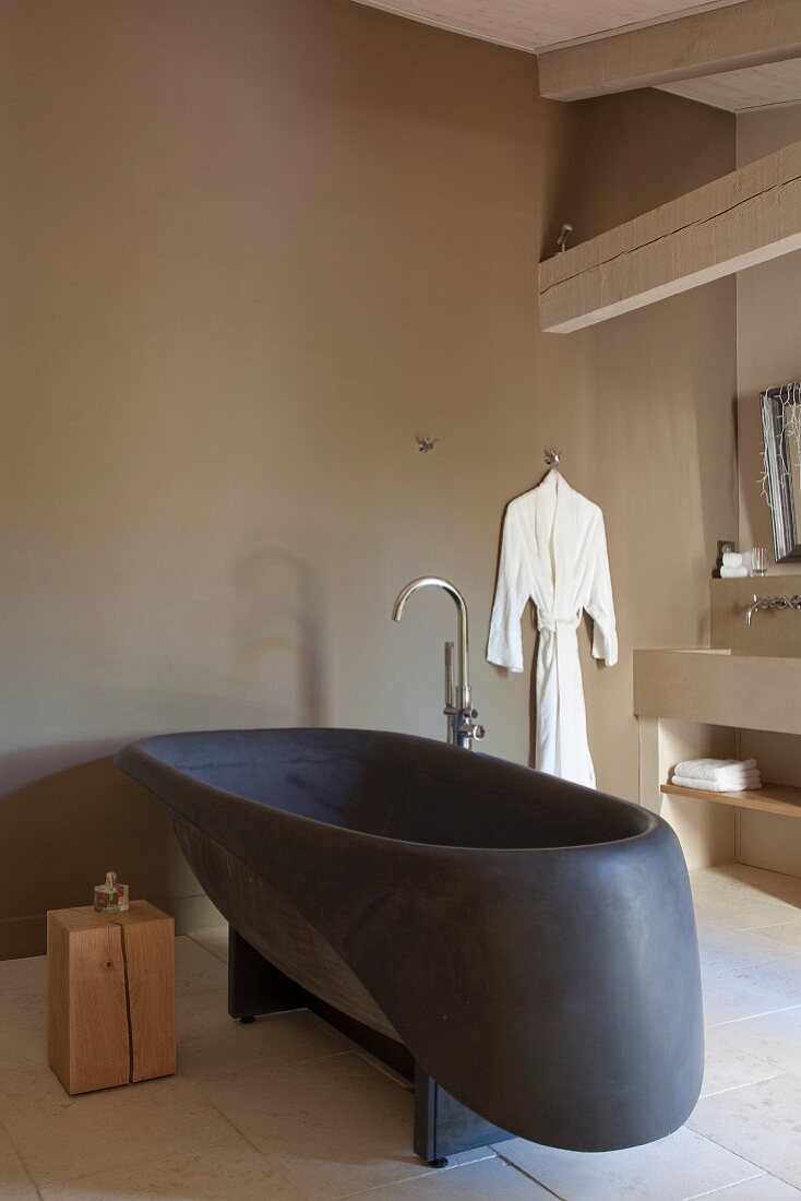 Schwarze Designerwanne und Holzblock als Ablage in puristischem Bad