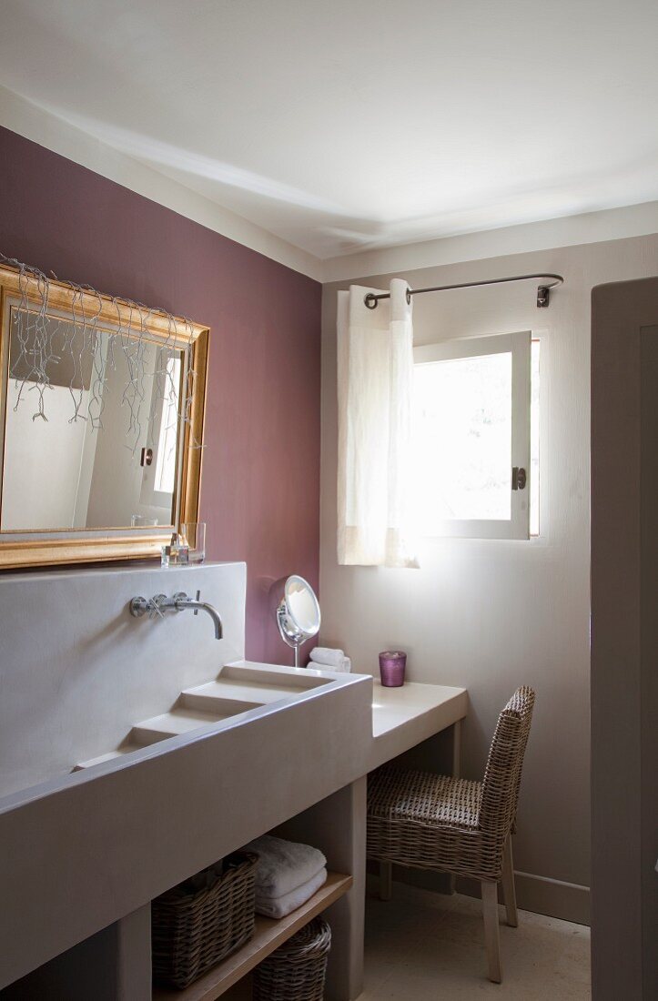 Concrete cascade sink on washstand below gilt-framed mirror on wall painted mauve