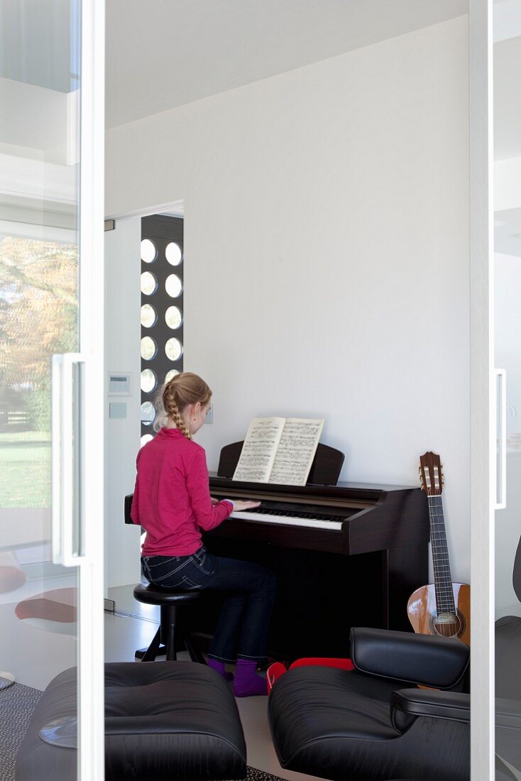 View through open sliding door of girl playing piano in music room
