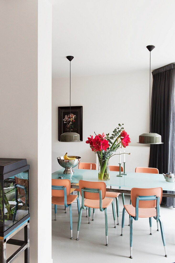 Flowers on dining table and wooden chairs with metal frames below two pendant lamps with metal lampshades