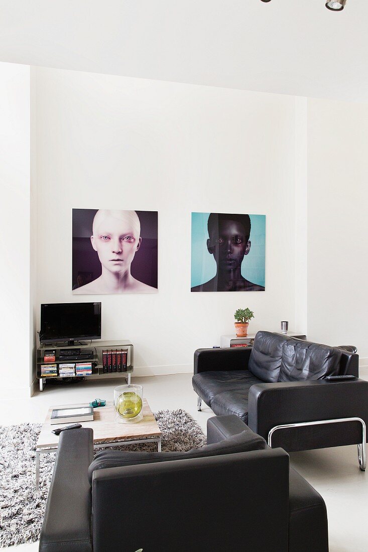 Schwarze Ledersofagarnitur mit Sessel um Couchtisch, im Hintergrund grossformatige Portraits an Wand, in minimalistischem Ambiente