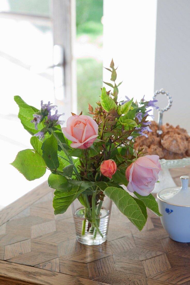 Roses in vase of garden flowers on table