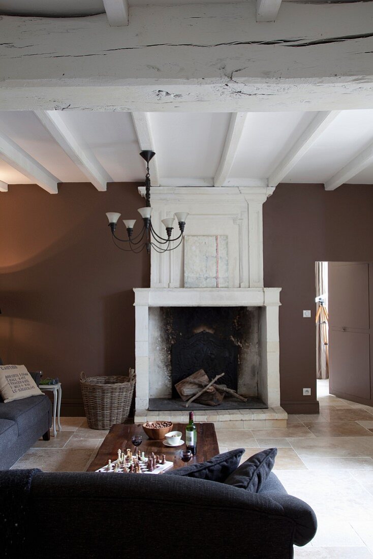 Rustic interior with open fireplace, comfortable sofa, wall painted dark brown and white, wood-beamed ceiling