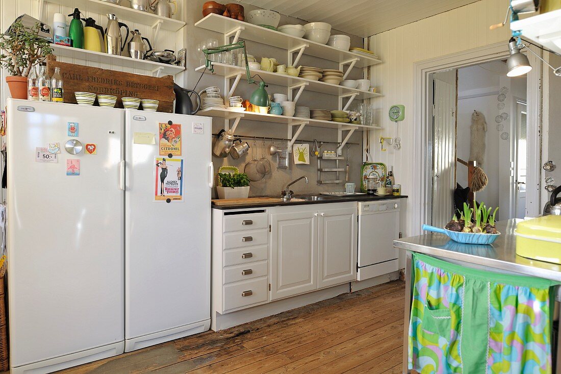 Küchenzeile mit weissen Unterschränken und Wandkonsolen mit Geschirr, seitlich Kühlschankkombination in schlichter Landhausküche