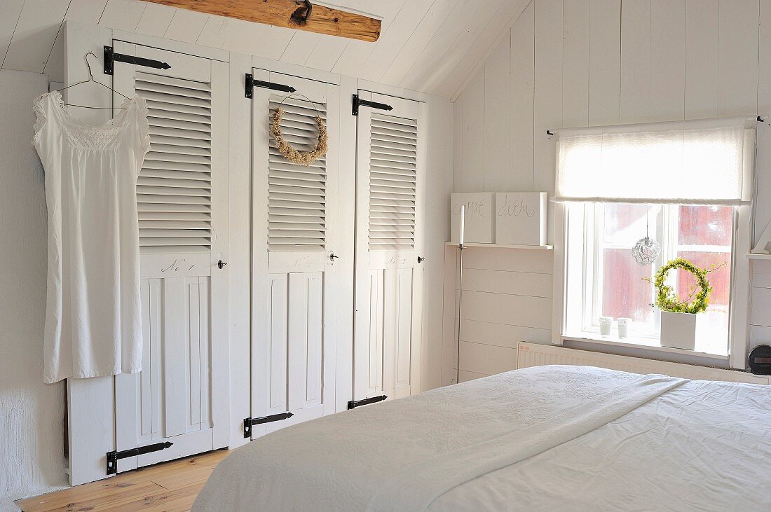 Simple, country-house bedroom with white fitted wardrobes, white wall cladding and Scandinavian vintage ambiance