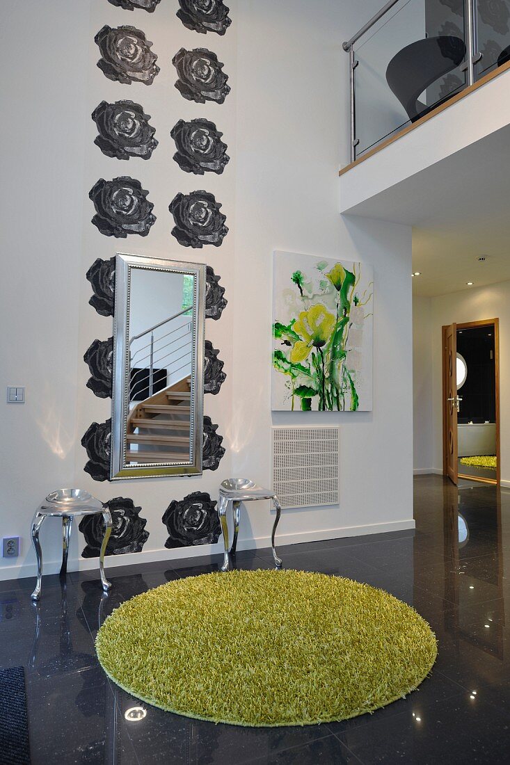 Florales Wandmotiv im offenen Wohnraum, davor postmoderne Hocker, Spiegel und grüner Hochflorteppich