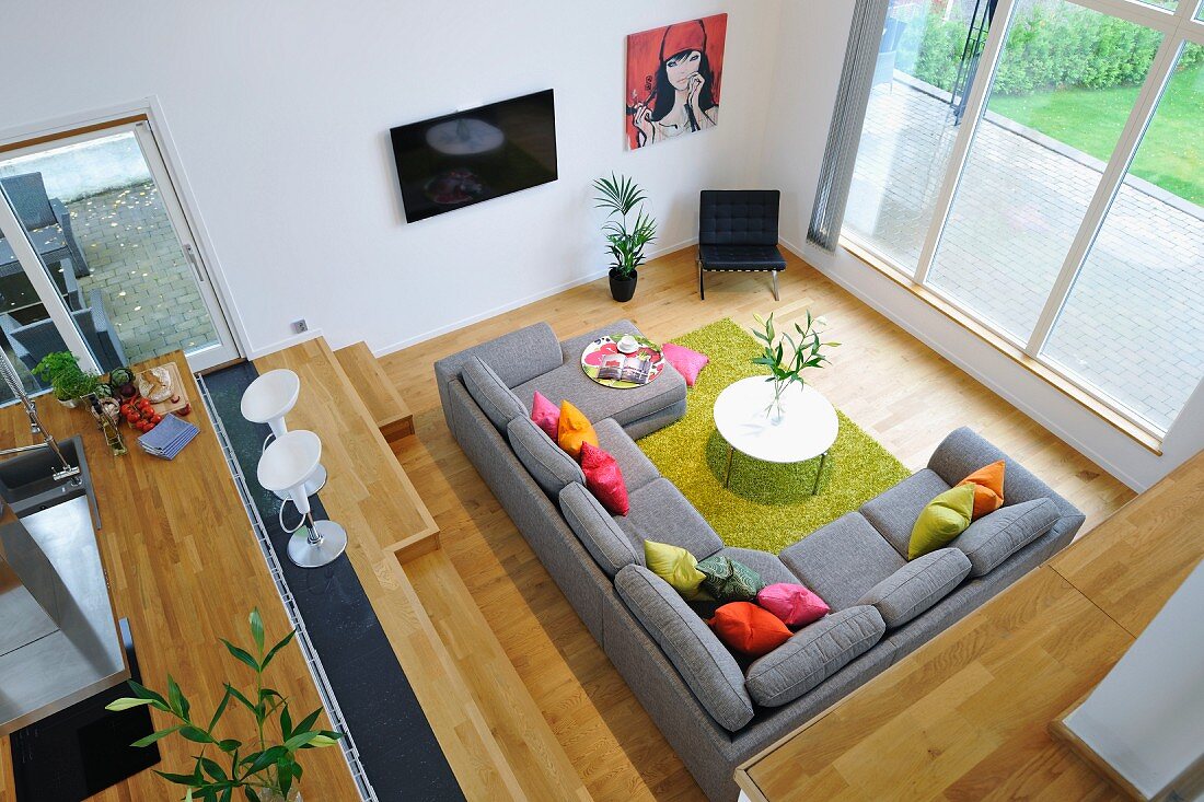 View from gallery down onto grey sofa combination with colourful scatter cushions and green rug surrounded by pale wooden surfaces
