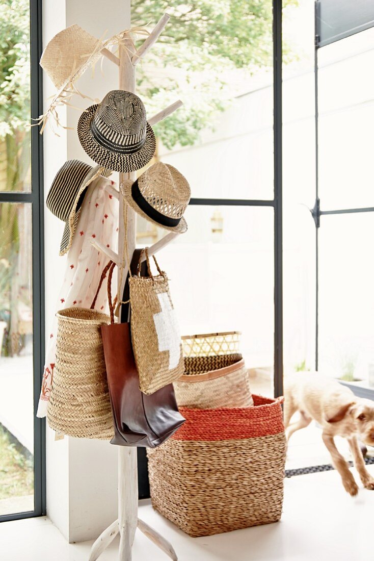 Baumartiger Garderobenständer mit Hutsammlung, dahinter gestapelte Körbe, neben offener Terrassentür und Blick in Garten